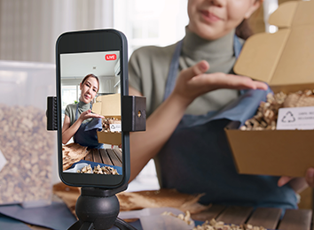 Mädchen präsentiert vor der Smartphone-Kamera einen offenen Karton mit umweltfreundlicher Verpackung.