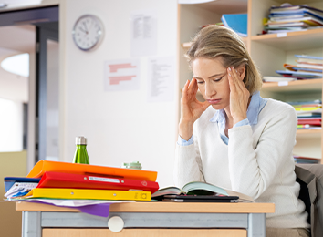 Lehrkraft an Pult reibt sich die Schläfen