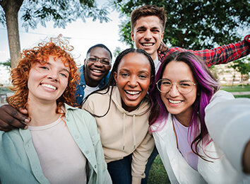Gruppe fröhlicher Jugendlicher macht draußen ein gemeinsames Selfie und lächelt in die Kamera.