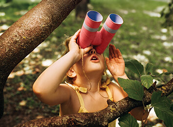 Kleines Mädchen schaut im Wald durch eine selbst gebastelte Papprohr-Fernglas in die Ferne