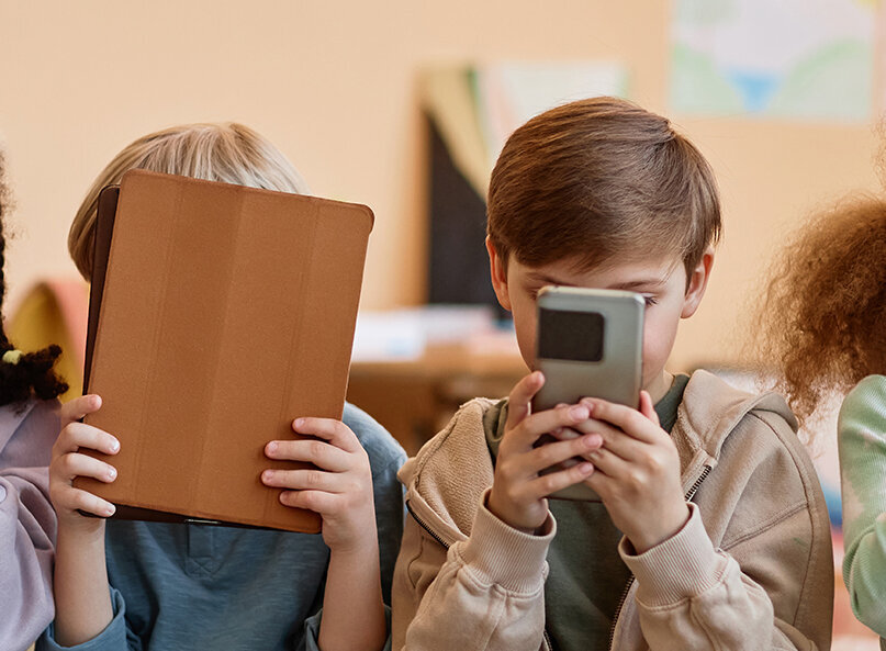 Vier Kinder sitzen nebeneinander und halten Smartphones oder ein Tablet vor das Gesicht.