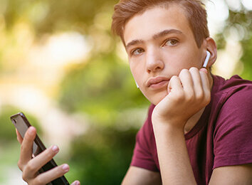 Zum Beitrag: Ist Vorsicht besser als Nachsicht? Nachdenklicher Junge mit Kopfhörern und Smartphone