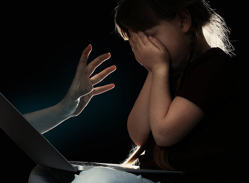 Kind vor Laptop, verdeckt das Gesicht, symbolisch für Online-Gefahren.