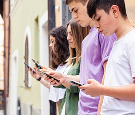 Vier Jugendliche stehen nebeneinander an einer Hauswand und blicken auf ihre Smartphones.