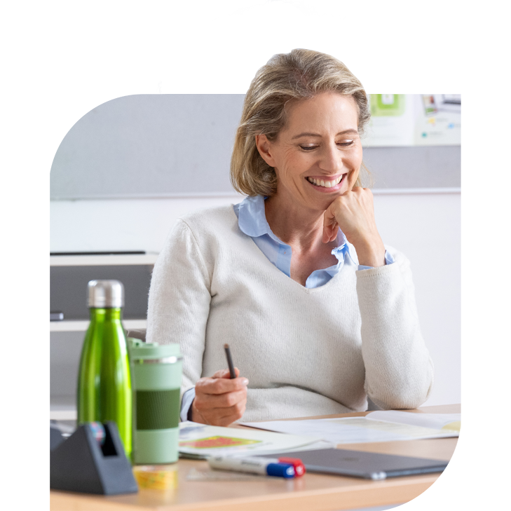 Frau sitzt lächelnd am Schreibtisch mit ausgebreiteten Unterlagen