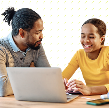 Vater spricht mit seiner Tochter die lächelnd am Laptop arbeitet.